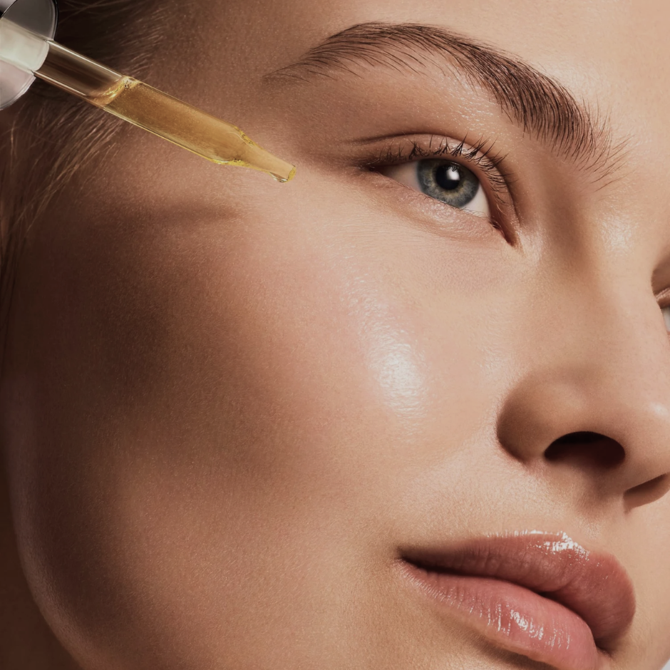 Close-up of a woman's face with a dropper applying a substance to her eyebrow.